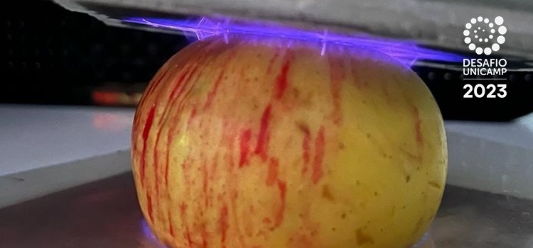 Foto colorida de uma maça recebendo o plasma frio, que parecem raios roxos. Fim da descrição.