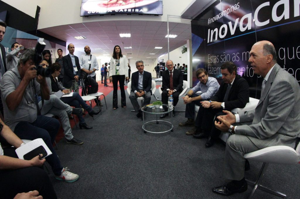 Executivos sentados em círculo e debatendo com painel de InovaCampinas ao fundo