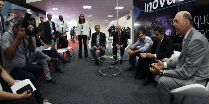 Executivos sentados em círculo e debatendo com painel de InovaCampinas ao fundo
