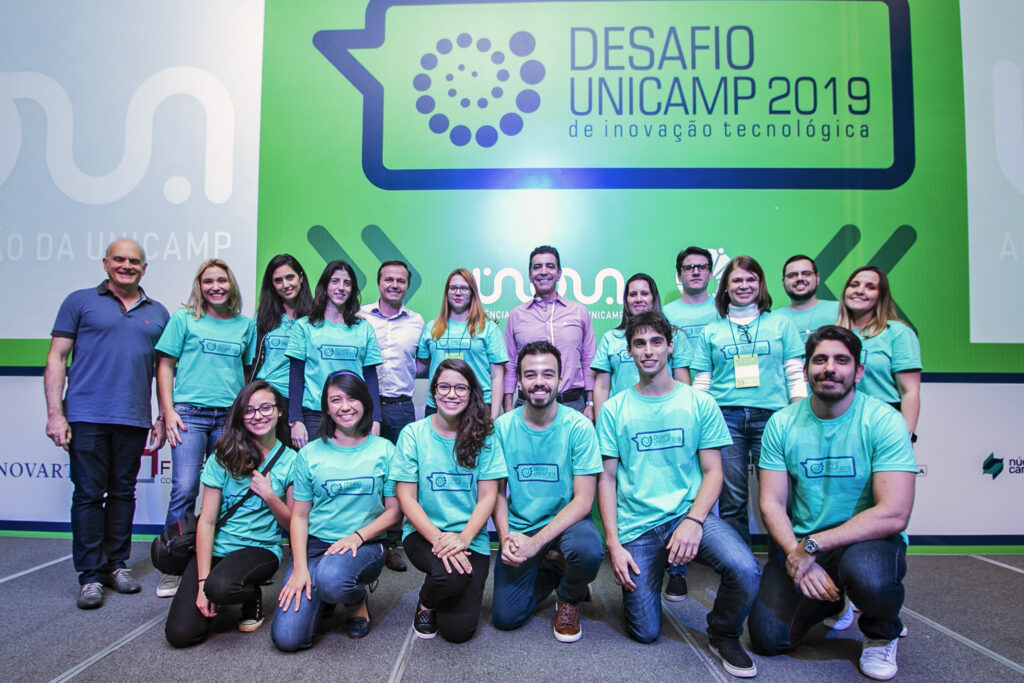 18 pessoas da Inova Unicamp em frente ao painel verde com logo do Desafio Unicamp