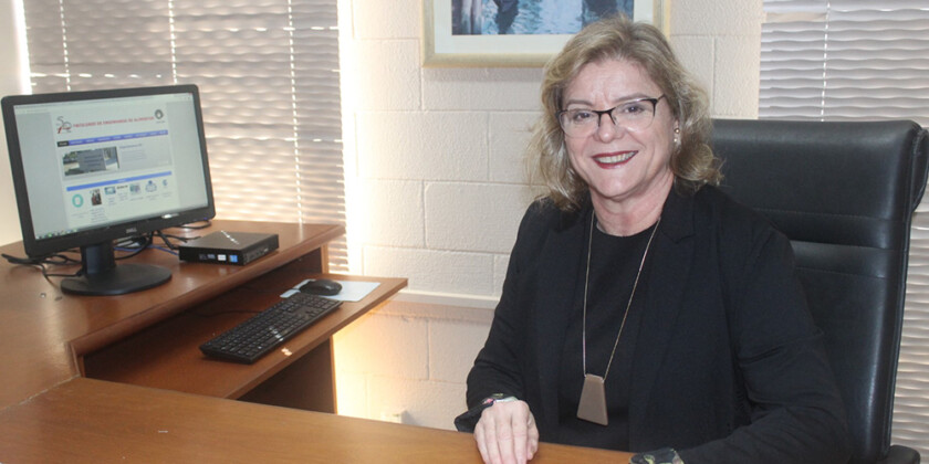 Prof. Mirna Gigante, diretora da FEA, está sentada sorrindo em seu escritório