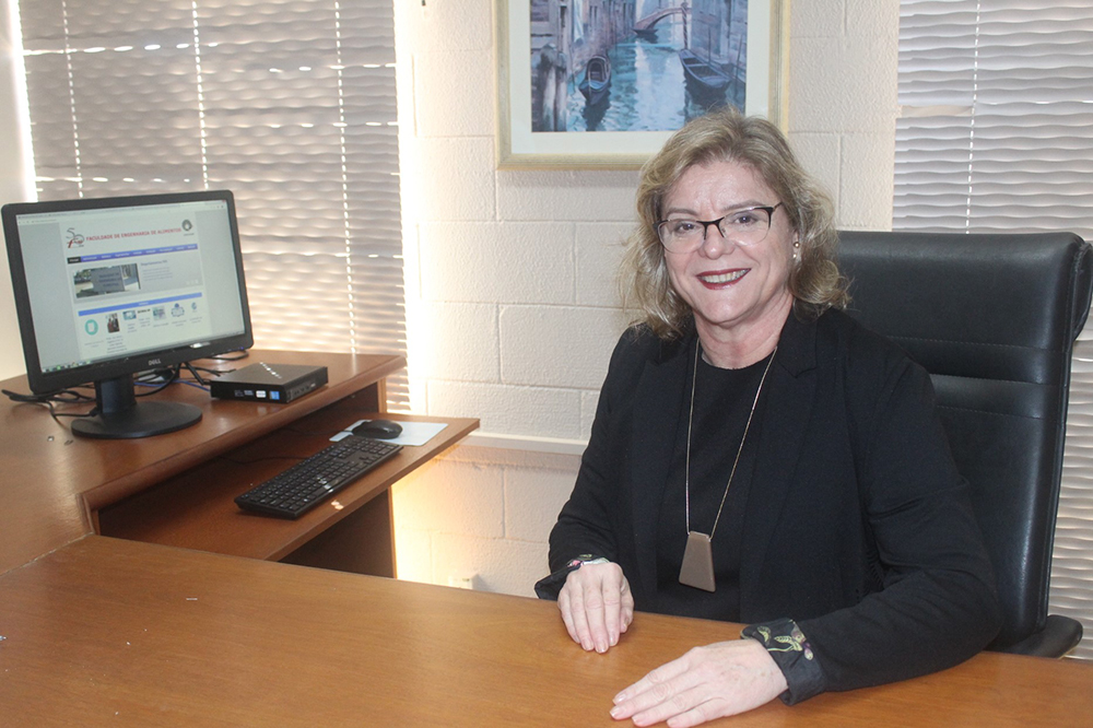 Prof. Mirna Gigante, diretora da FEA, está sentada sorrindo em seu escritório