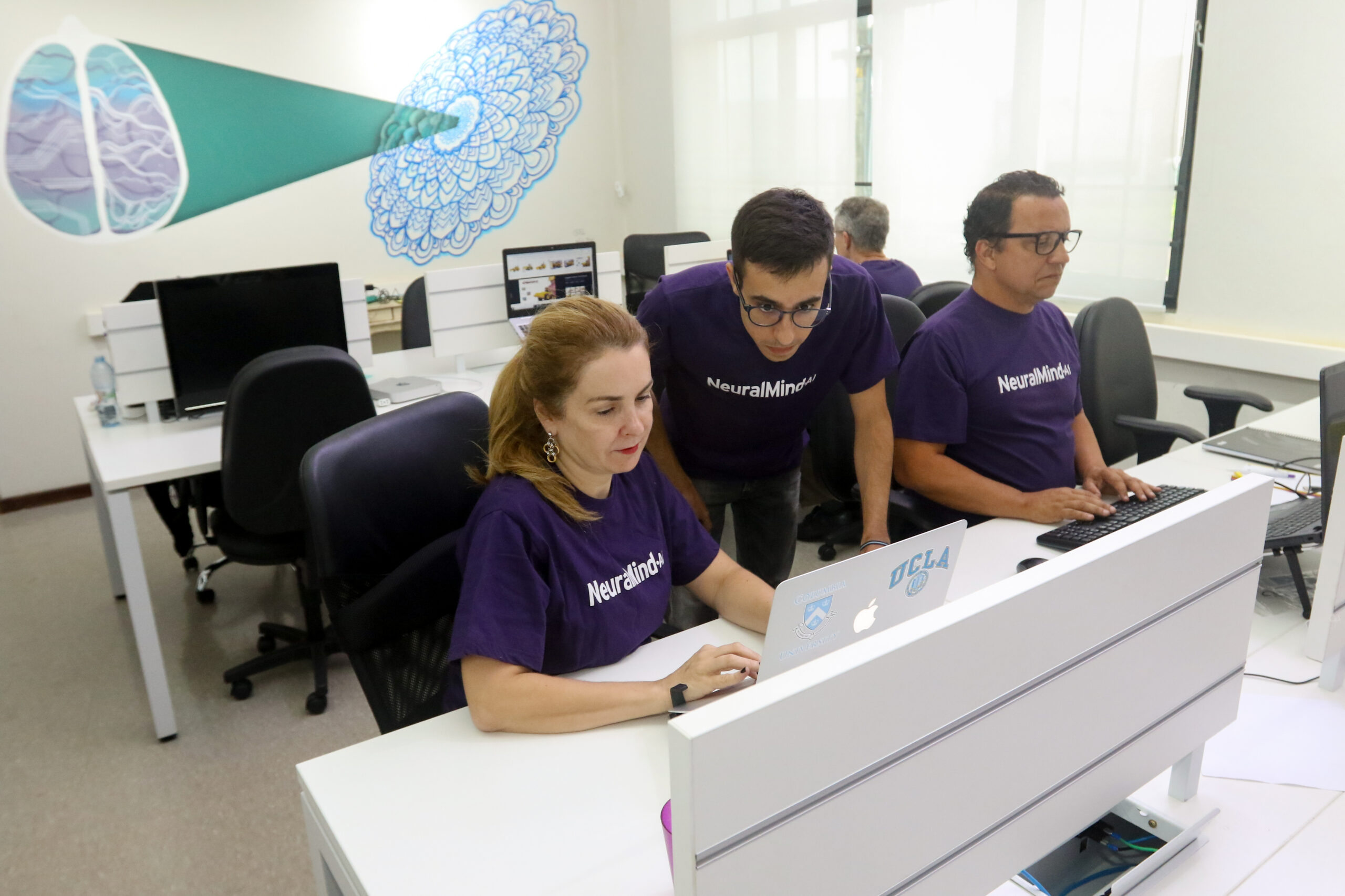 Laboratório da NeuralMind com computadores e 4 funcionários trabalhando