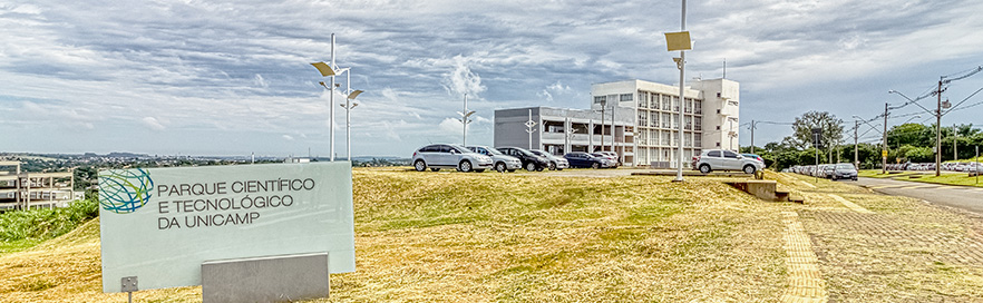Na foto, está em primeiro plano a placa do Parque Científico e Tecnológico da Unicamp e ao fundo carros estacionados e os prédios Soma e Núcleo, duas unidades que hospeda empresas com projetos de P&D na Unicamp.