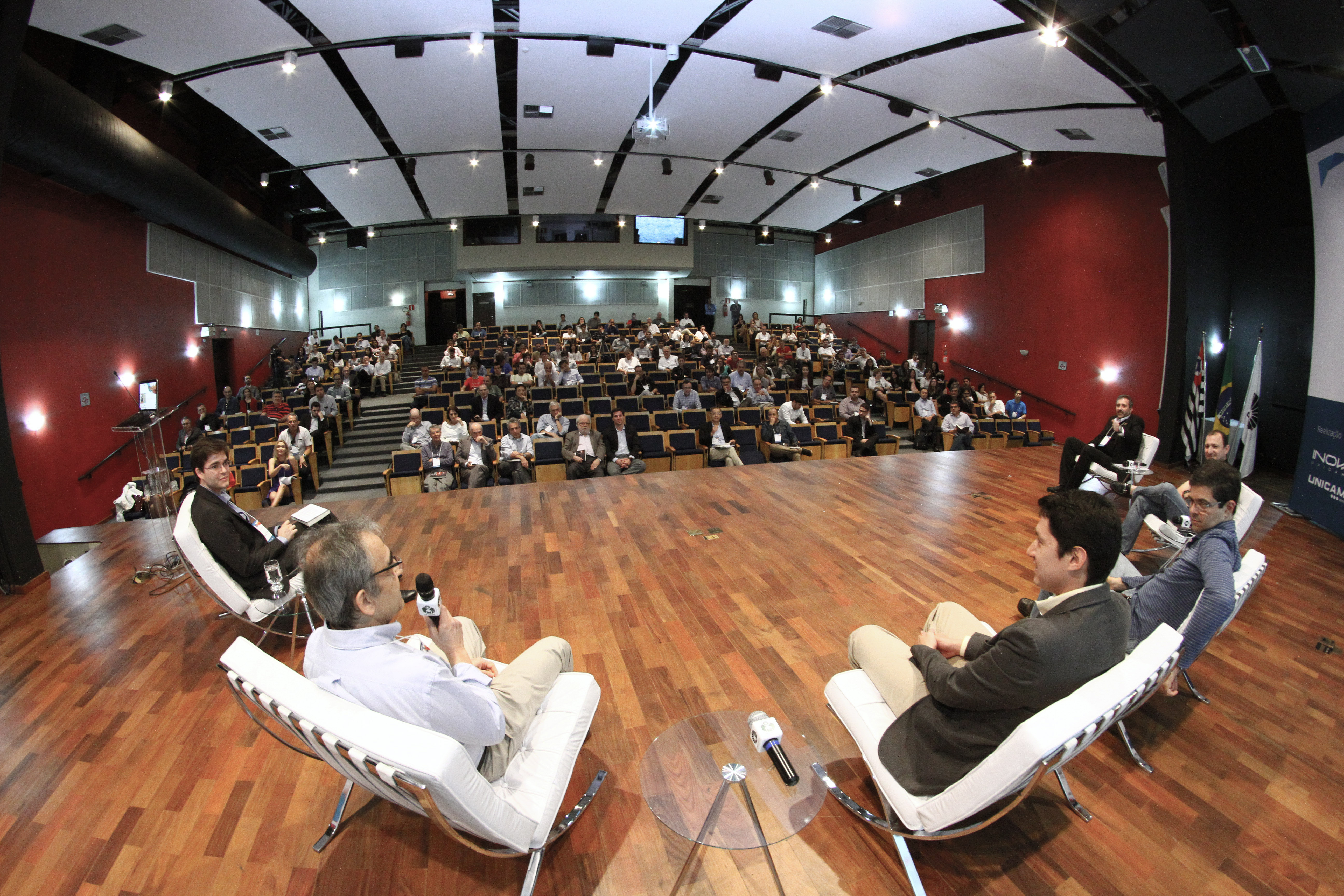 Cinco pessoas sentadas debatendo no palco de um auditório com plateia