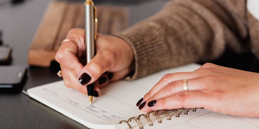 A imagem foca na mão de uma mulher escrevendo um uma agenda.