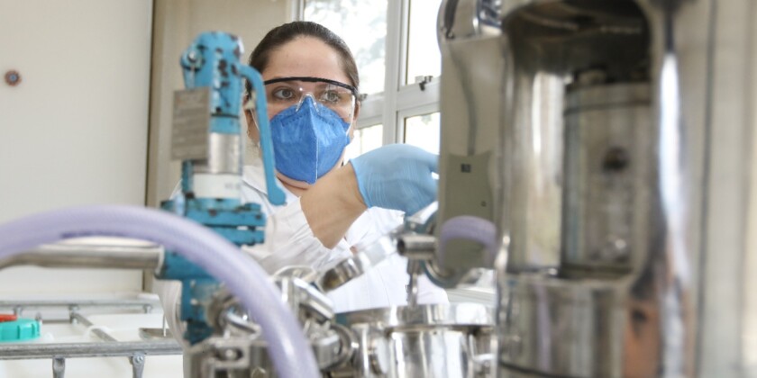 Pesquisadora mulher com máscara e luvas azuis mexe em equipamentos em laboratório de pesquisas