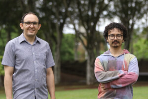 A foto mostra dois homens: O professor Tiago Fernandes Tavares (à esquerda) e o pesquisador Gustavo Nishihara (à direita). Os dois homens estão próximos e olhando para a câmera. É possível ver ao fundo algumas árvores, em um ambiente de jardim.