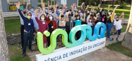 grupo de incubados da Incamp e investidores em área externa, na frente do letreiro da Inova Unicamp, todos estão de mão levantada
