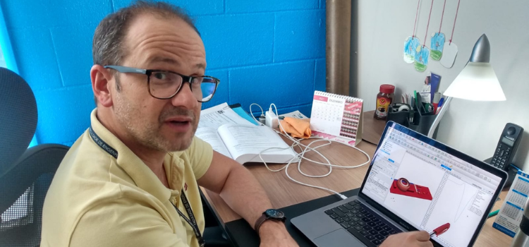 Professor Sávio Vianna sentado em uma cadeira de frente para um notebook que está com o software aberto. O professor usa óculos, é um homem branco e está vestindo uma camisa polo amarela.