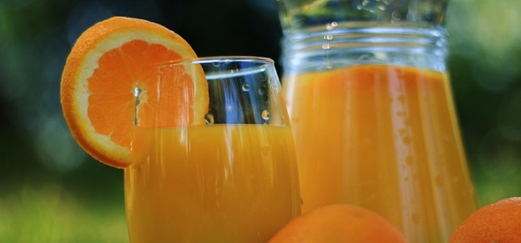 Um copo e uma jarra de vidro transparentes com suco de laranja