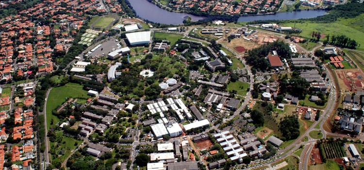 Foto aérea da Unicamp onde aparecem prédios, ruas e praças com foco no círculo do ciclo básico da universidade. fim da descrição