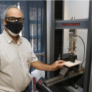 A imagem mostra um homem branco, por volta de 50 anos, operando uma máquina responsável pela produção das placas planas de concreto desenvolvidas na Unicamp. Fim da descrição.