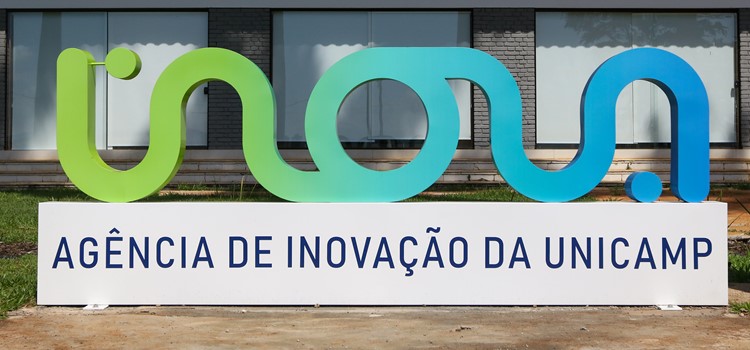 Foto colorida do totem do logotipo da Inova Unicamp em cores verdes e azuis, no qual está inscrito Inova Agência de Inovação da Unicamp. Fim da descrição.