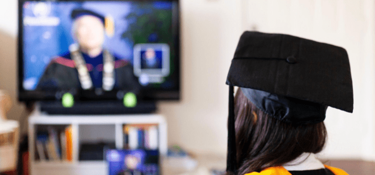 A imagem mostra uma estudante de costas, com um chapéu de formatura, sentada assistindo uma apresentação na televisão.