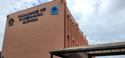 Foto da fachada da FEQ-Unicamp, um prédio cor terracota com o nome em letras azuis. Fim da descrição.