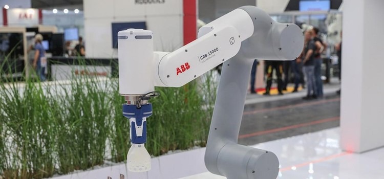Braço robótico em cores branco e cinza é apresentado em feira de exposições. Fim da descrição.