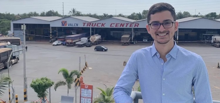 O CEO e fundador da DieselBank, Lucas Rodolfo, é um homem branco, jovem, que usa óculos, veste camisa azul clara e posa para foto num pátio com caminhões ao fundo. Fim da descrição.