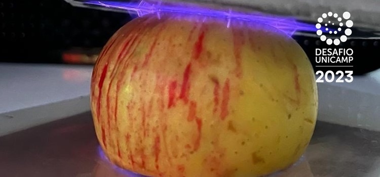 Foto colorida de uma maça recebendo o plasma frio, que parecem raios roxos. Fim da descrição.