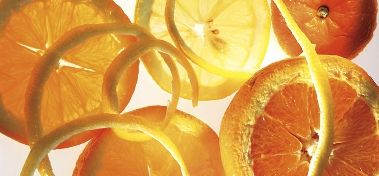 Pedaços de laranjas cortadas e casca de laranja em fundo branco. Fim da descrição.