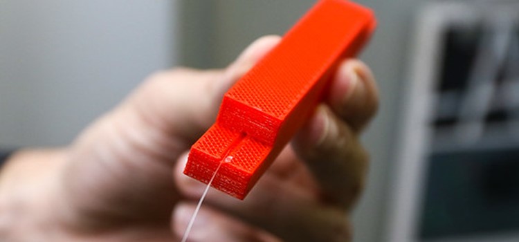 Foto do dispositivo, uma pequena caixa laranja por onde passa o fio da fibra óptica. Fim da descrição.