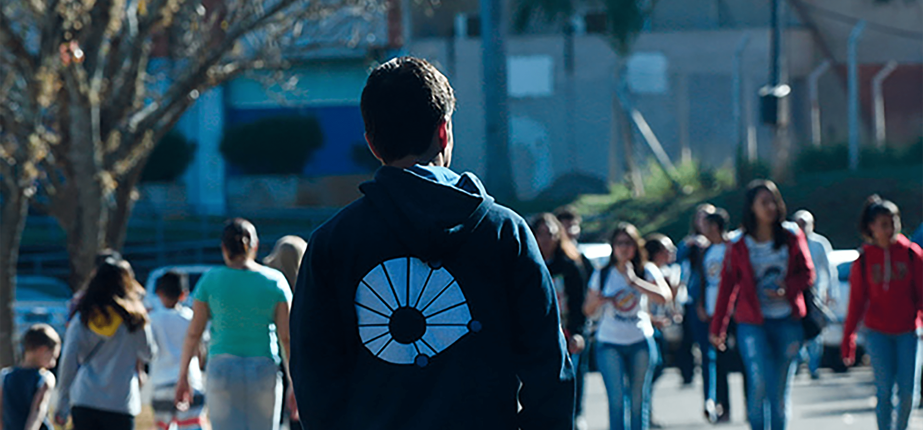 Foto com muita circulação de pessoas e foco em um rapaz caminhando com moletom com o logo da Unicamp nas costas. Fim da descrição