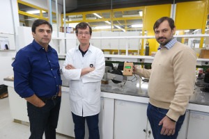 Foto colorida de três pesquisadores em ambiente de laboratório com bancadas e equipamentos ao fundo. Fim da descrição.