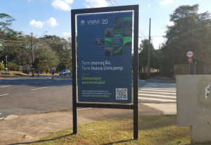 Foto de banner da campanha "Tem inovação, tem inova Unicamp" posicionado em cruzamento do campus da Unicamp em Campinas. Fim da descrição.