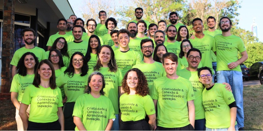 A imagem mostra o grupo de novos incubados posando para a foto. Todos estão utilizando uma camiseta verde com os seguintes dizeres: criatividade e conexão e aprendizado e inovação. Fim da descrição.