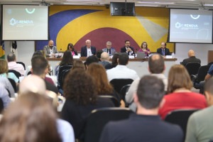 Imagem do autidório da FEQ mostra pessoas sentadas de costas e no segundo plano a mesa diretiva com as autoridades. Fim da descrição