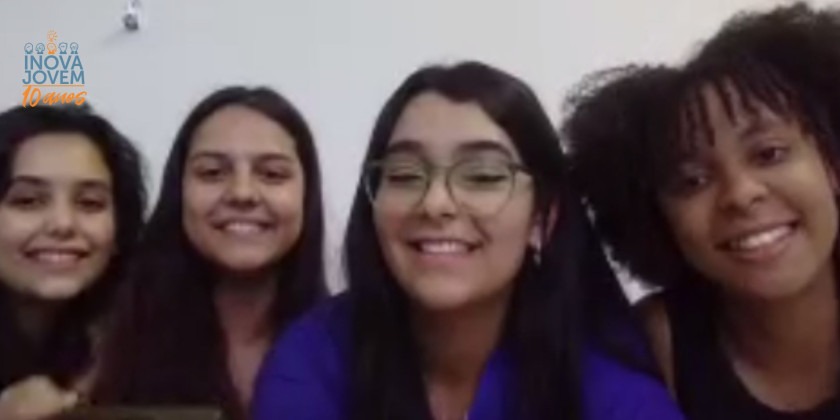 Captura de tela. Quatro meninas, três brancas e uma negra sorriem para a câmera.