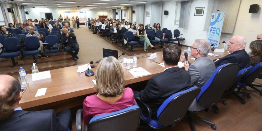 Foto de auditório lotado. As pessoas assistem às falas das autoridades que estão na mesa central. Fim da descrição.