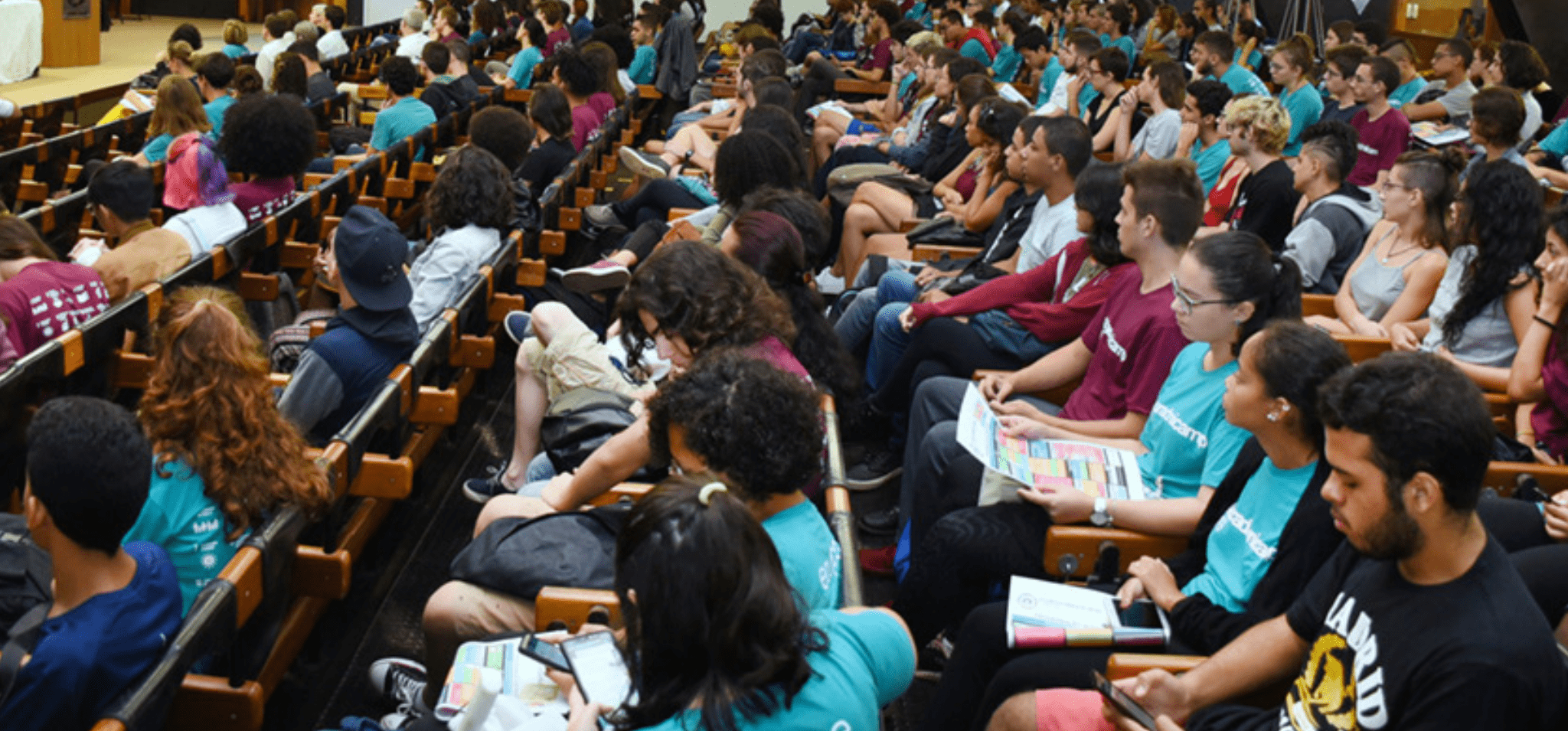 Foto colorida de centenas de alunos sentados em auditório da Unicamp, na recepção da calourada da Universidade. Fim da descrição.