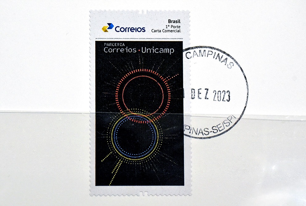 Imagem do selo postal criado pelos Correios para marcar a parceria a Unicamp. O selo é um pequeno retângulo e conta com o texto "Parceria Correios e Unicamp". 