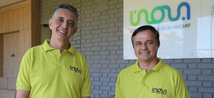 Os professore Renato Lopes e Rangel Arthur posam para foto com camiseta polo verde-limão com o logotipo da Inova Unicamp e em frente a um painel com o logotipo da Inova Unicamp. Fim da descrição.